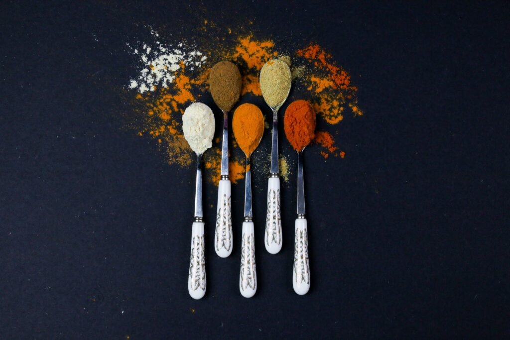 Top view of assorted spices on decorative spoons placed on a dark background for culinary inspiration.